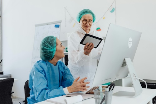 Two medical professionals in protective gear collaborate using a tablet.