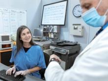 Healthcare worker in scrubs smiling at a masked medical professional.